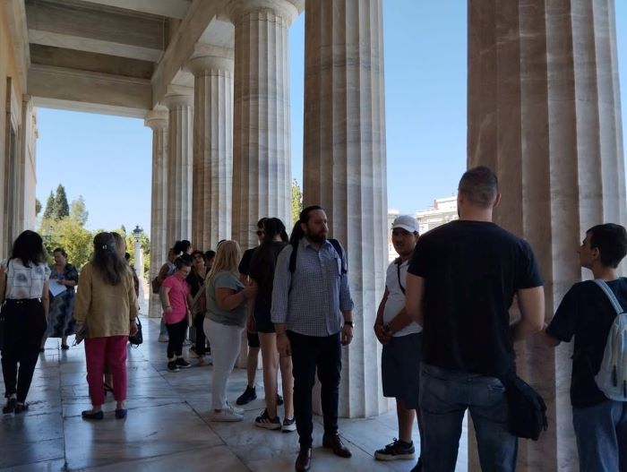 Μαθητές και συνοδοί στον προαύλιο χώρο της Βουλής, κάποια παιδιά αγγίζουν τους μαρμάρινους κίονες που υπάρχουν στην πρόσοψη της Βουλής.