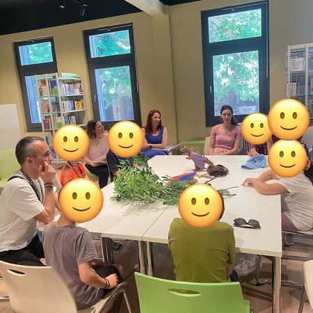 ωφελούμενοι και συνοδοί με προσωπικό της βιβλιοθήκης γύρω από τραπέζι στο οποίο διακρίνονται αντικείμενα που σχετίζονται με την πολυαισθητηριακή αφήγηση του παραμυθιού “Οι περιπέτειες του  Πρίγκιπα Ζίγκφριντ”